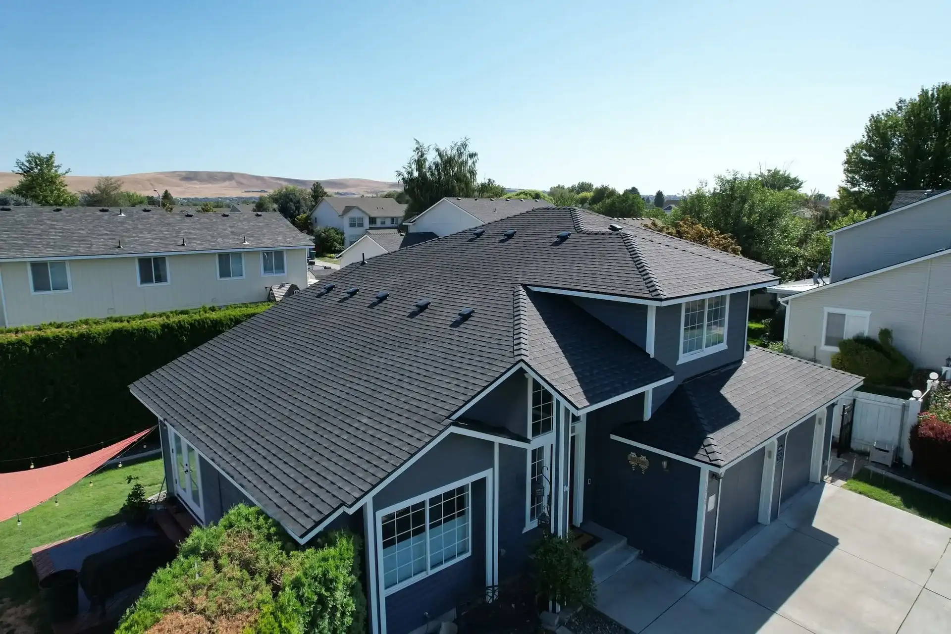Navy two-story home with a new charcoal architectural shingle roof installed by Pantoja's Construction, seen from a drone