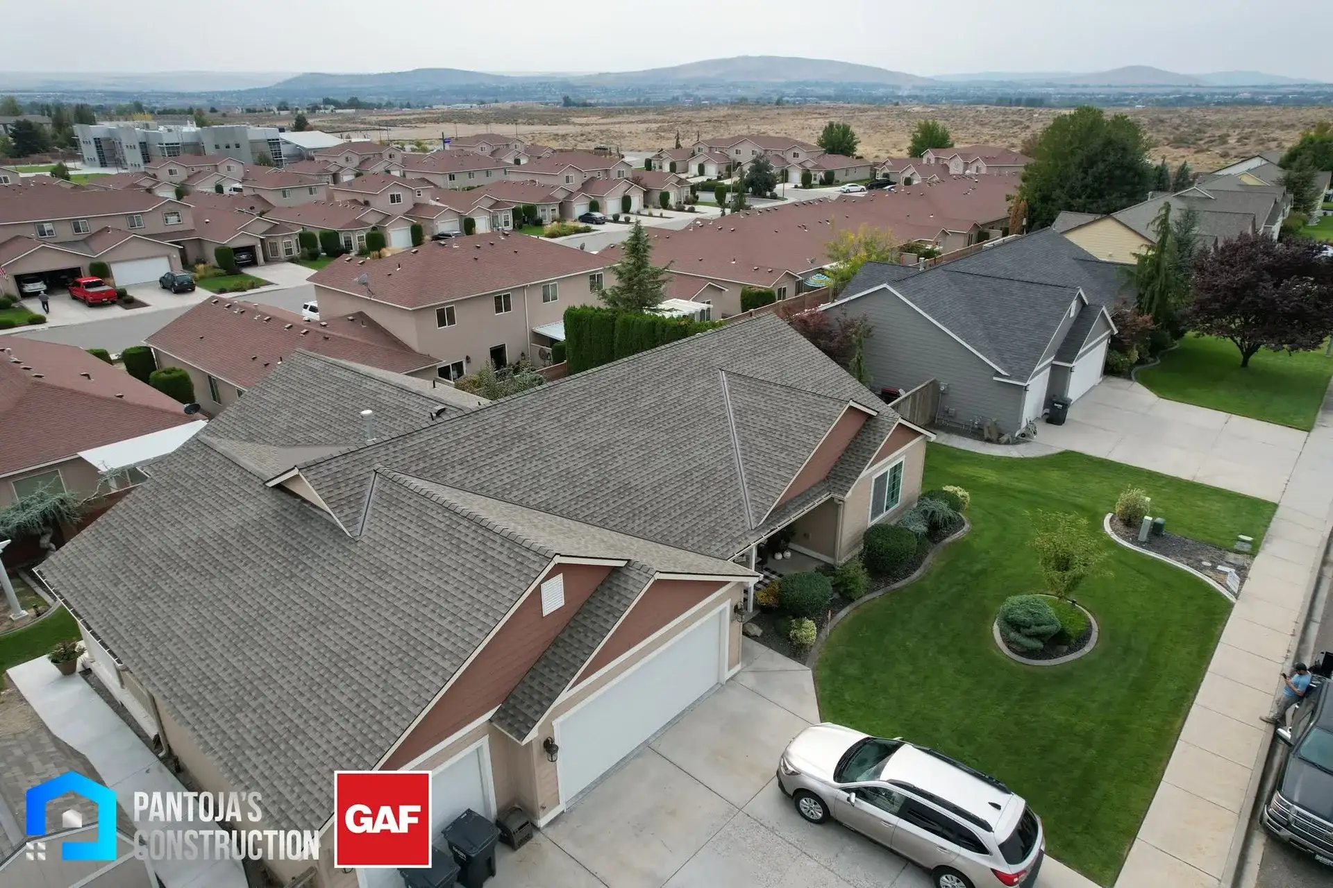 Vista de dron de una casa con techo nuevo de teja arquitectónica GAF instalado por Pantoja's Construction, con el vecindario y los cerros detrás